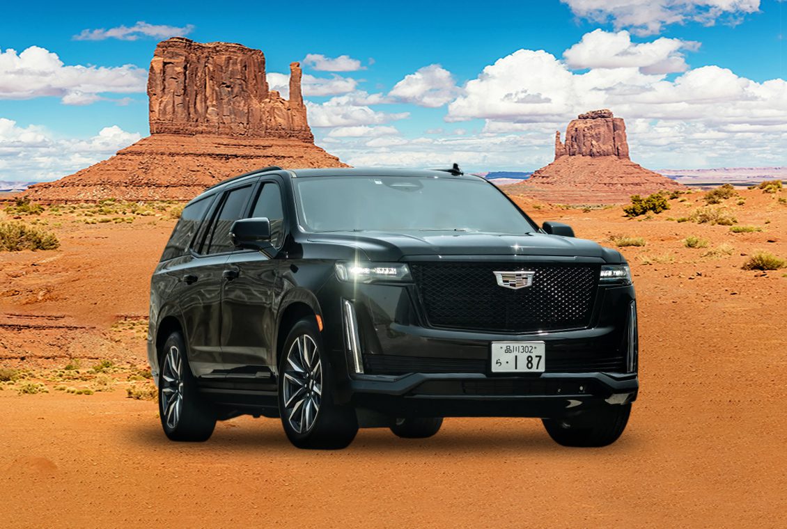A sleek black Cadillac SUV parked in a desert landscape with iconic rock formations.